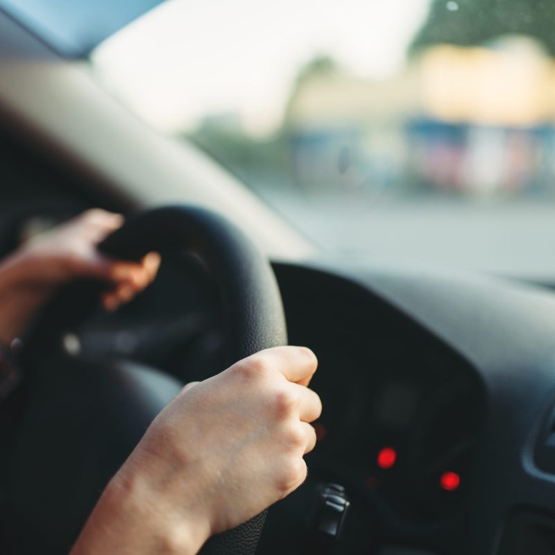 Female car driver beginner clung to the wheel, driving school concept. Automobile exam or test on the street